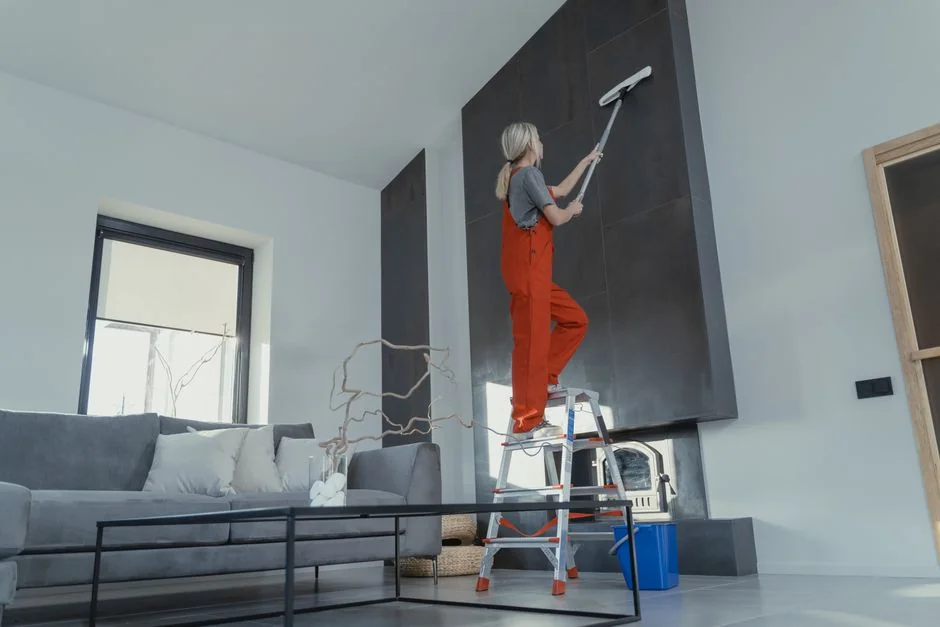 A woman cleaning the floor with a vacuum cleaner while a dog watches attentively. Indoor home setting.