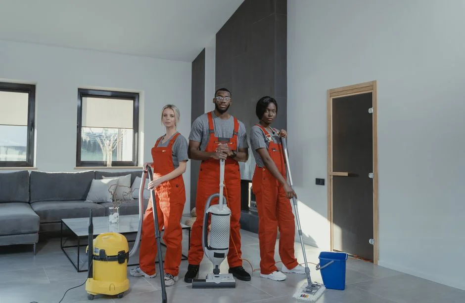 An adult woman in red coveralls operates a vacuum cleaner in a modern indoor setting, focusing on cleaning tasks.